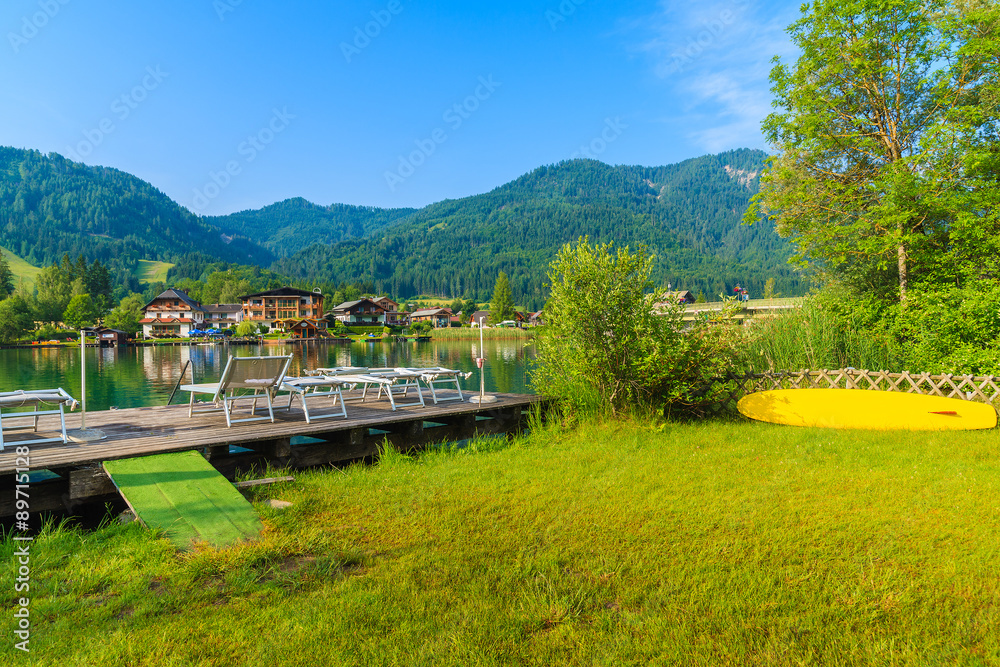 Fototapeta premium Sunbeds on wooden pier on shore of Weissensee lake in summer landscape of Carinthia land, Austria