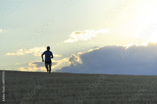 frontal silhouette of young man running in countryside training in summer sunset