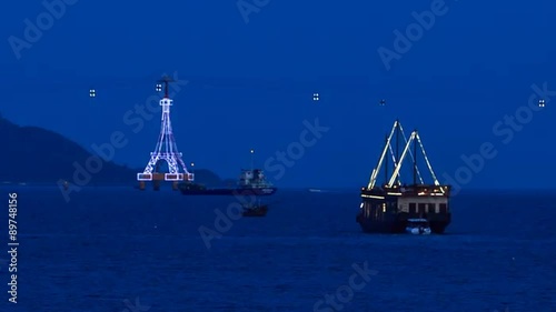 drifting ship along bay at night against ropeway and lightship