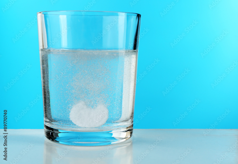 Pill in glass of water on blue background Pill in glass of water on blue background