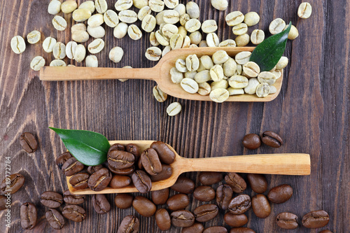 Green and brown coffee beans with spoons on wooden table close up
