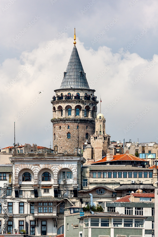 View of the Galata Tower in Istanbul, close-up. Turkey. In the foreground, the old houses, the minaret. On the tower are the tourists. Sunny day. Blue sky with clouds.