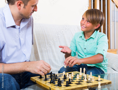 Man and teenager son playing chess.