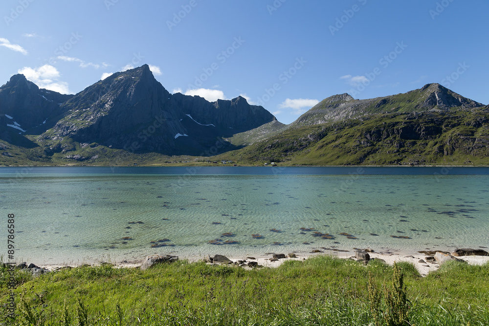 A beach with mountains in the background crystal clear water and some clouds