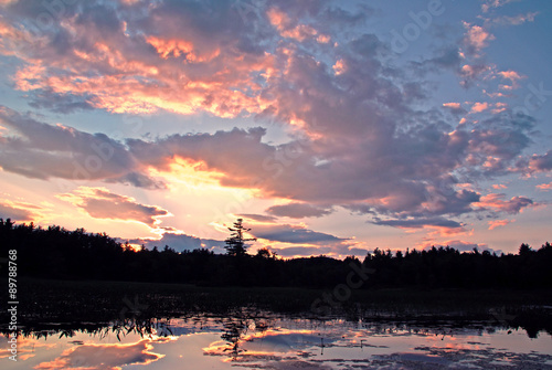 Sunset illumines the sky and plays on the pristine surface of a scenic Maine lake, adding reflections and ripples to the beauty of the scene. photo