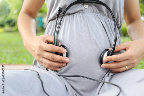 Pregnant women put earphone in hand on her belly.