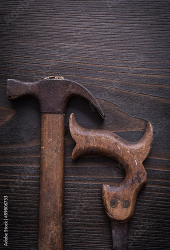 Rusty handsaw and claw hammer on vintage wooden background