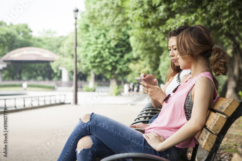 Two young women talking while watching the mobile phone in a park bench © Monet