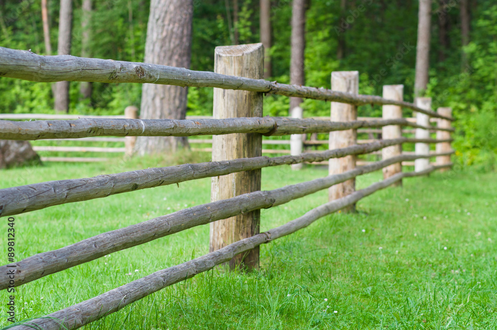 Rural wooden fence with green lawn, part of farm cattle-pen