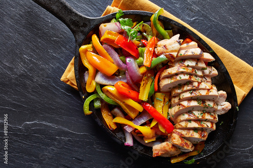 mexican grilled chicken fajitas in iron skillet shot from overhead on slate