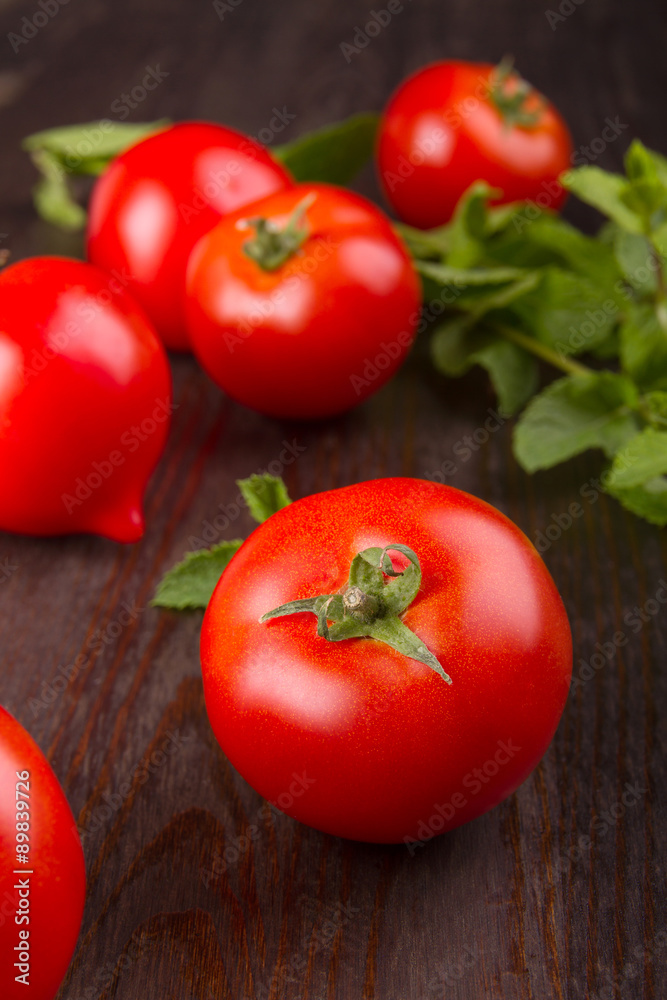 red tomato on a dark board surrounded by tomatoes and a sprig of mint red tomato on a dark board surrounded by tomatoes and a sprig of mint