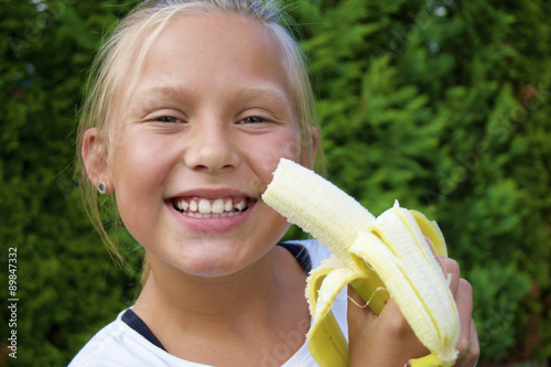 Fröhliches, lachendes Mädchen isst eine Banane