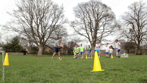 Adults on grassed area with school children supervising a football training session, Everyone can be seen running around cones. School building can be seen in the background. photo