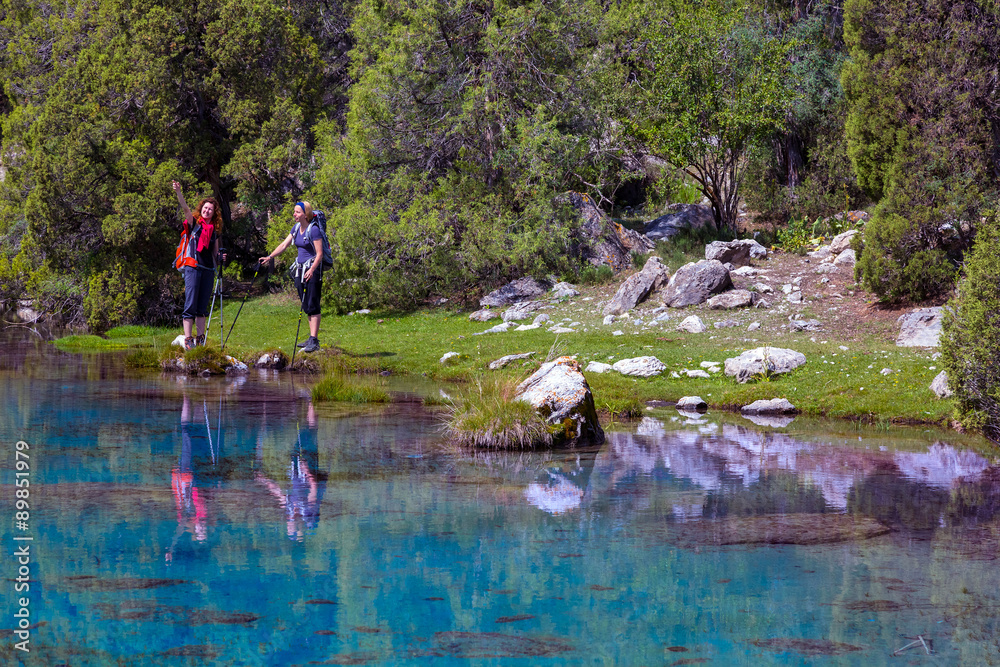 Pristine mountain lake Group of hikers walks along the shore of mountain lake with vivid blue green turquoise colors and reflection of forest pine-trees and mountain valley