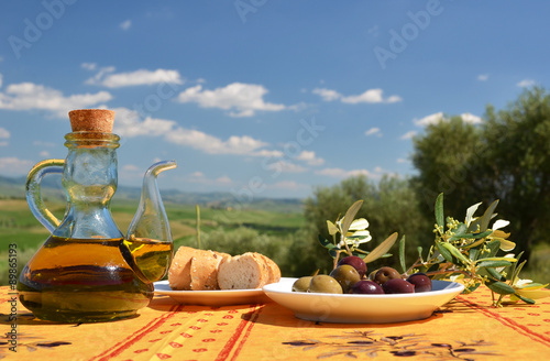 Olive oil, olives and bread on the table against Tuscan landscap