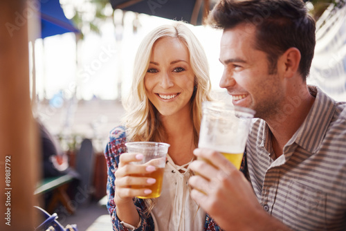 Fototapeta romantic couple drinking beer together in outdoor beach side pub or bar