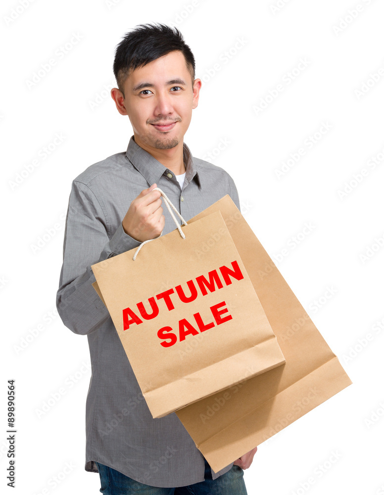 Asian man hold with shopping bag and showing autumn sale Asian man hold with shopping bag and showing autumn sale