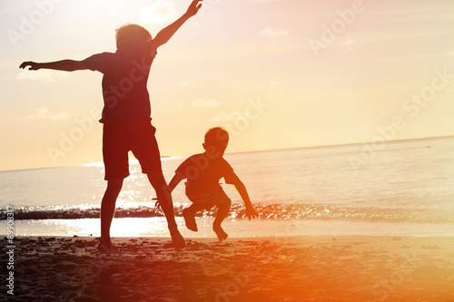 father and son jumping at sunset beach