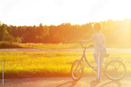 little boy riding bike in summer park at sunset