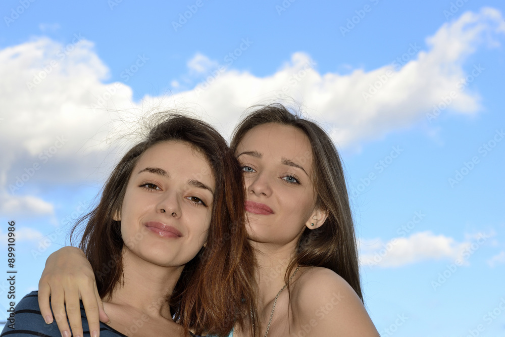 Two beautiful young women standing over blue sky and hugging Two beautiful young women standing over blue sky and hugging