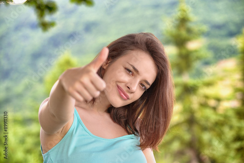 Beautiful young woman giving thumbs up sign in the mountains