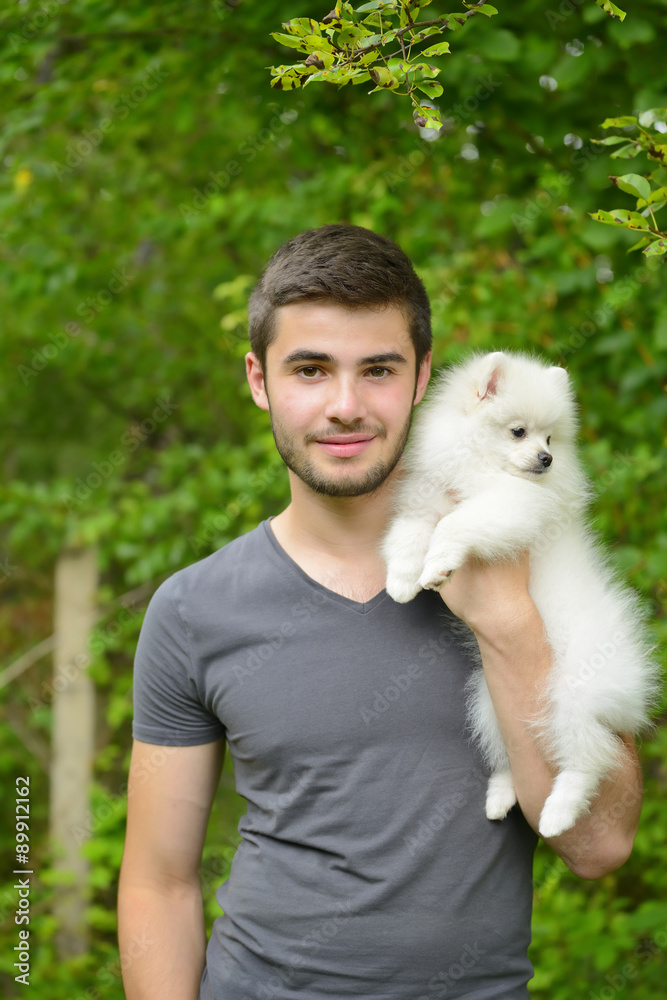 Attractive young man holding german spitz puppy outside and looking at camera. Attractive young man holding german spitz puppy outside and looking at camera.
