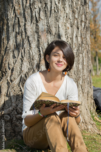 Beautiful young woman reading a book on tree background