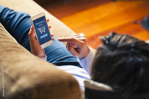 Woman shopping by mobile phone laying at home. Blue screen. She is laying on the sofa.