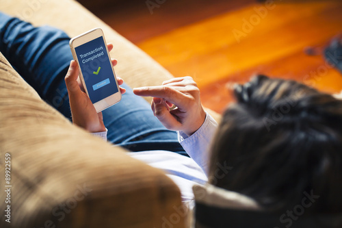 Woman using on line banking on mobile phone at home. Blue screen. She is laying on the sofa. photo