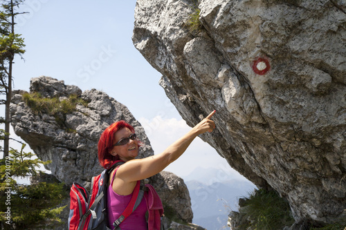 Pretty middle aged woman hiker pointing to the sign post on big mountain rock photo