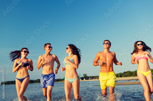 smiling friends in sunglasses running on beach