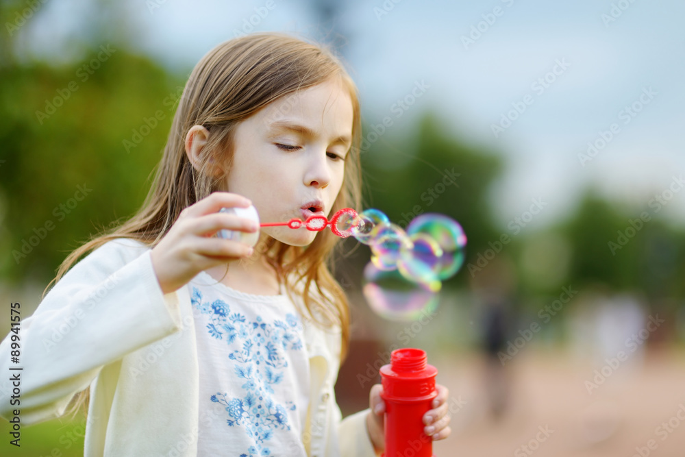 Funny lovely little girl blowing soap bubbles outdoors