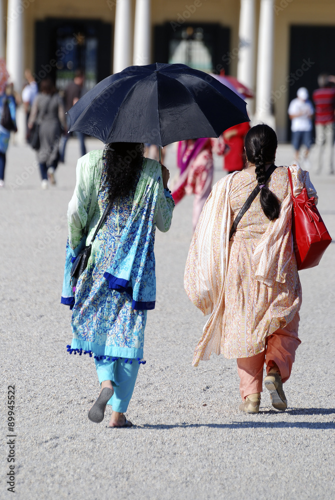 Traditionell gekleidete indische Frauen mit Regeschirmen als Sonnenschutz gehen auf den Hintereingang des Schlosses Schönbrunn in Wien zu.