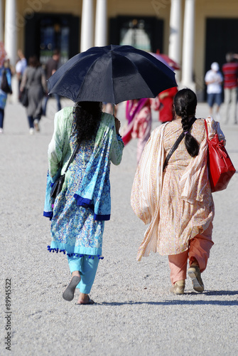 Traditionell gekleidete indische Frauen mit Regeschirmen als Sonnenschutz gehen auf den Hintereingang des Schlosses Schönbrunn in Wien zu.