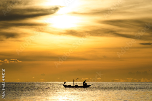 silhouette of fishermen in the boat on sea with yellow and orange sun in the background