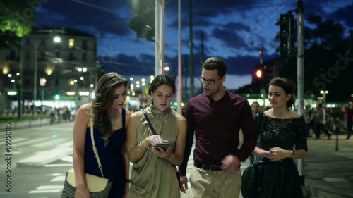 Friends walking and using smartphone at night in the city, steadycam shot
