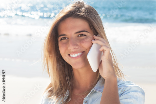 Frau mit blonden Haaren telefoniert am Strand