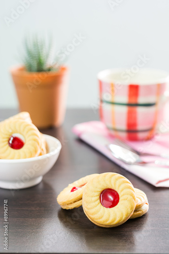 Sandwich cookies with cream and strawberry flavoured jam on wood