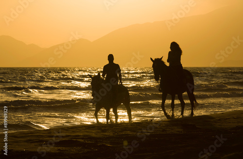 Horse rider couple at sunset beach, next to the sea
