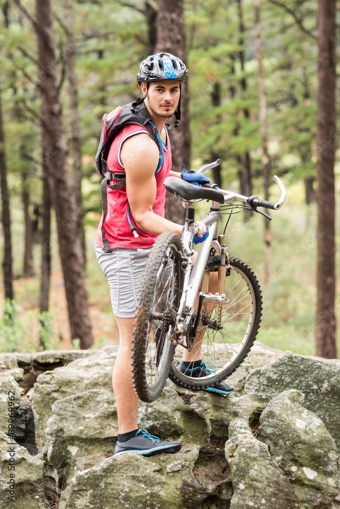 Young happy biker holding bike on a rock looking at camera Young happy biker holding bike on a rock looking at camera