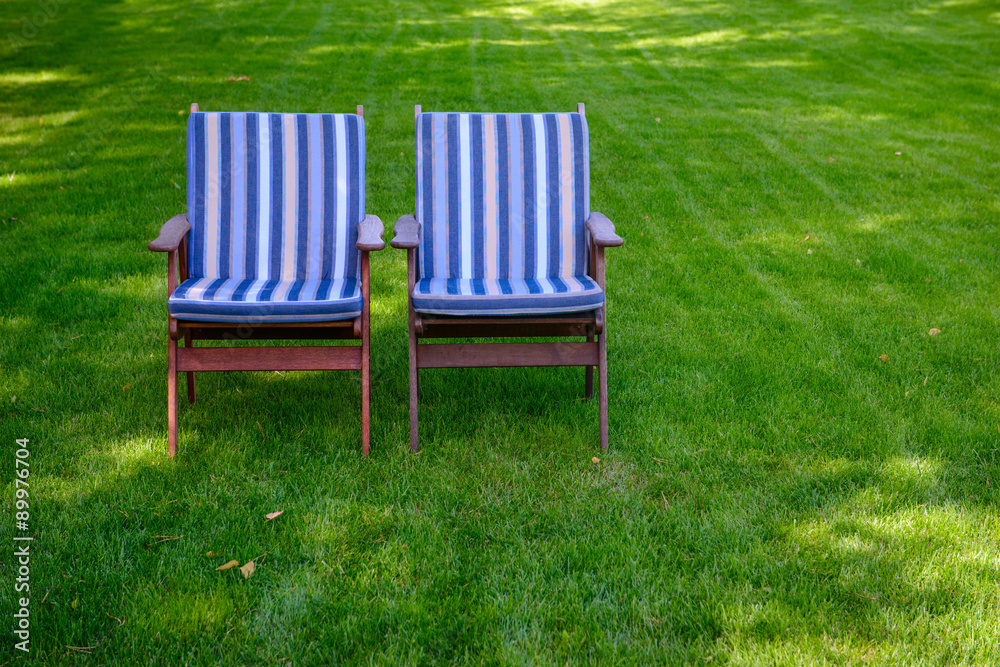 Two chairs with striped mattresses on a green grass