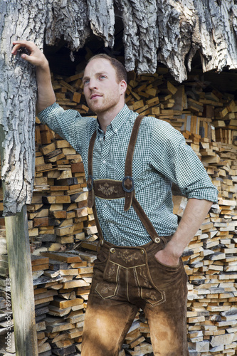 Quadro em tela young man in bavarian lederhosen in front of firewood