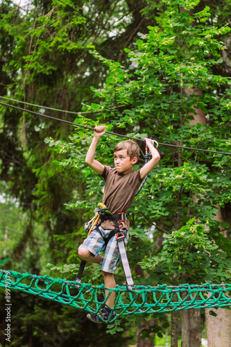 Boy climbing in adventure rope park in safety equipment