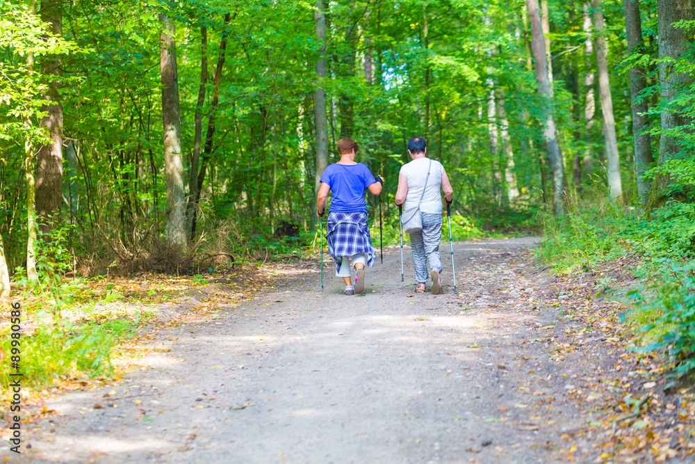 Two old womans nordic walking through forest path.