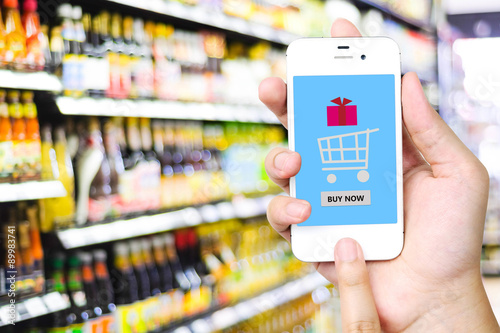 Buy now on smart phone screen over blur supermarket background,