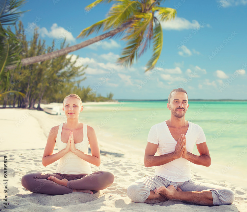 smiling couple meditating on tropical beach