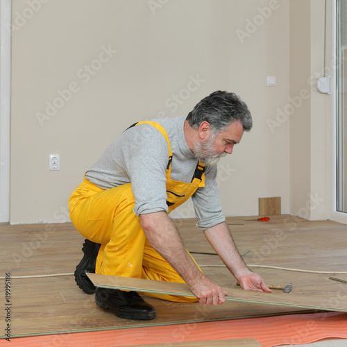 Laminate flooring of room, worker placing laminate plank 