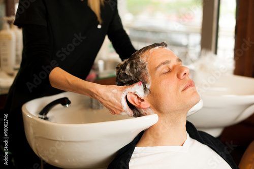 Female hairdresser washing hair of smiling man client at beauty