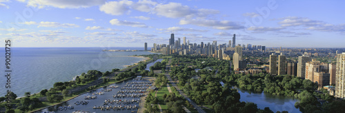 This shows Lincoln Park, Diversey Harbor with its moored boats, Lake Michigan to the left and the skyline in summer. There is morning light on the city.