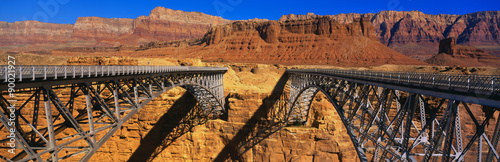 This is a Navajo Bridge that crosses the Colorado River. In the background are the Vermillion Cliffs of Red Rock. This is a double bridge made of steel.